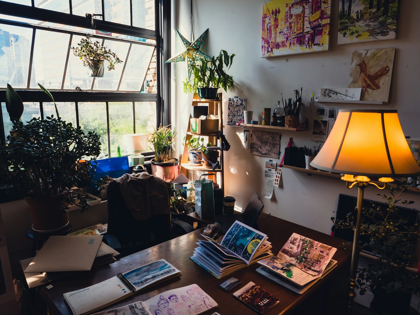 Art studio desk with sketchbooks, plants, and drawing tools.
