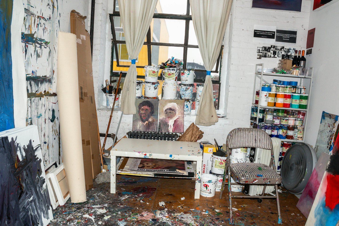 Paint splattered art studio floor with supplies and canvases.