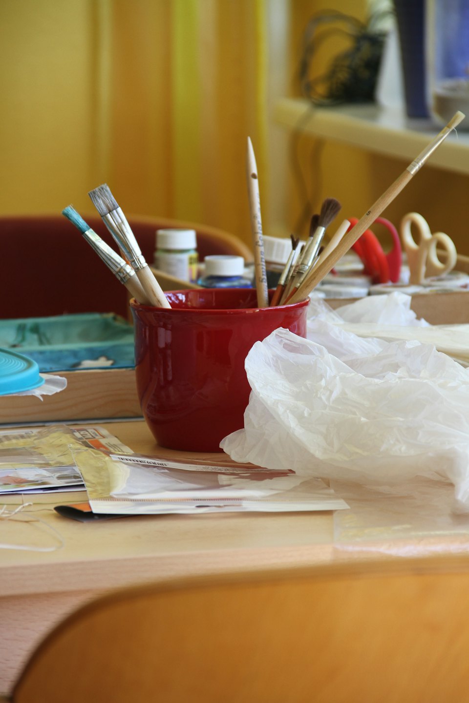 Paintbrushes and a wooden stylus sit in a ceramic mug.