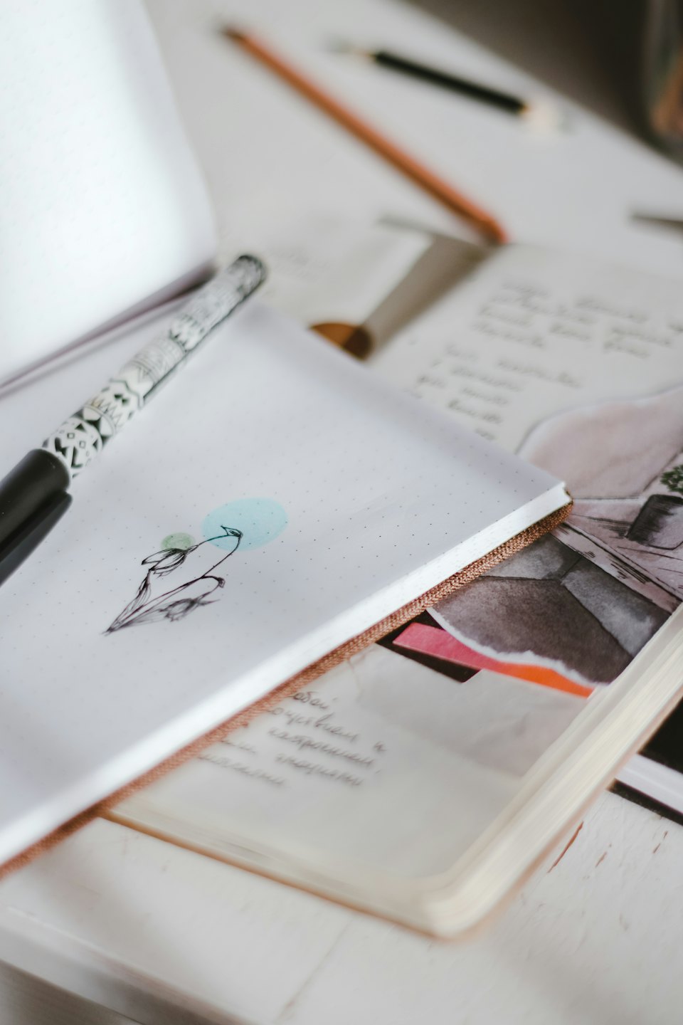 An open notebook displays a bird drawing beside a decorative pen.