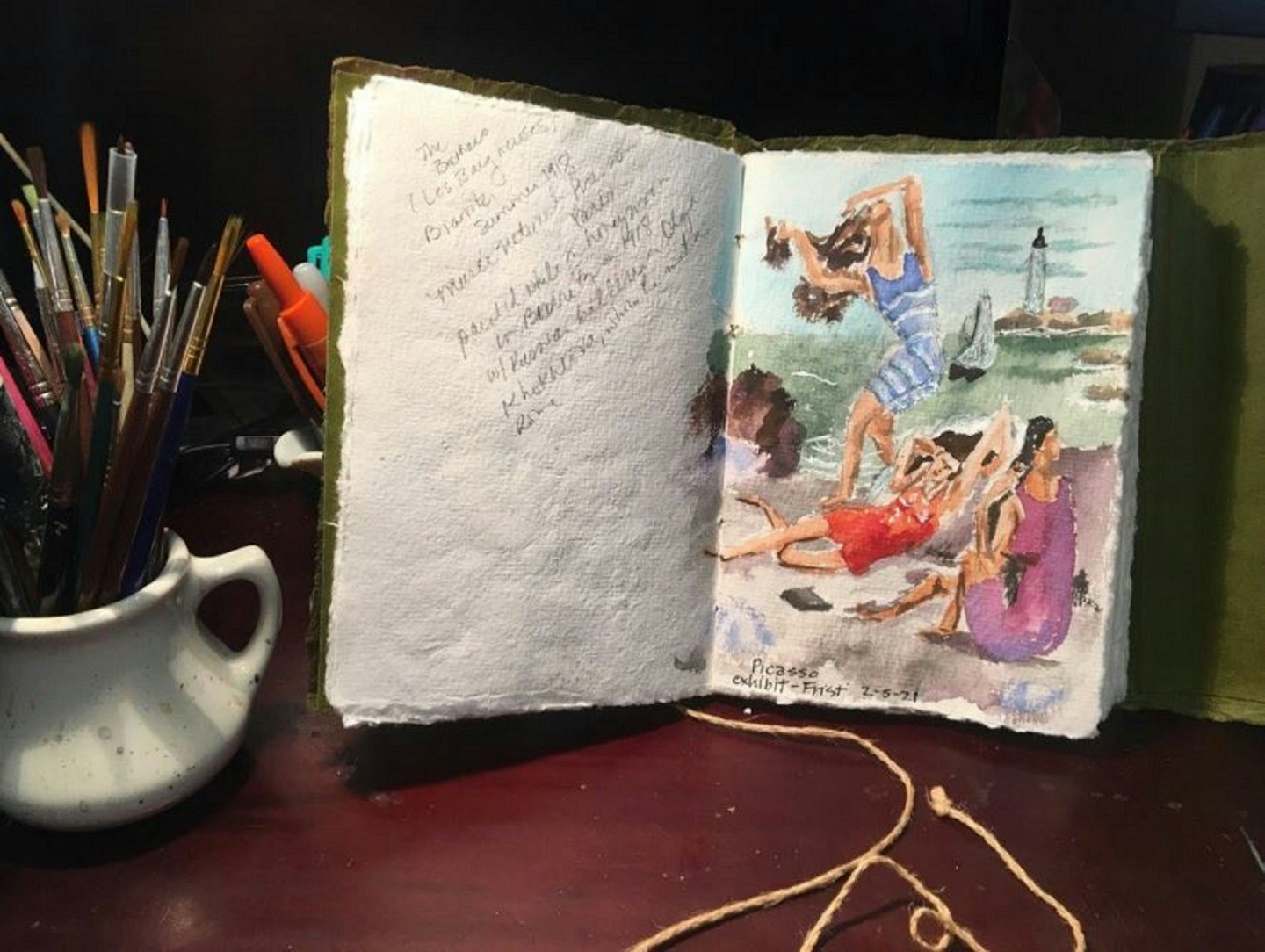 Handmade journal with watercolor paintings rests on a wooden desk.