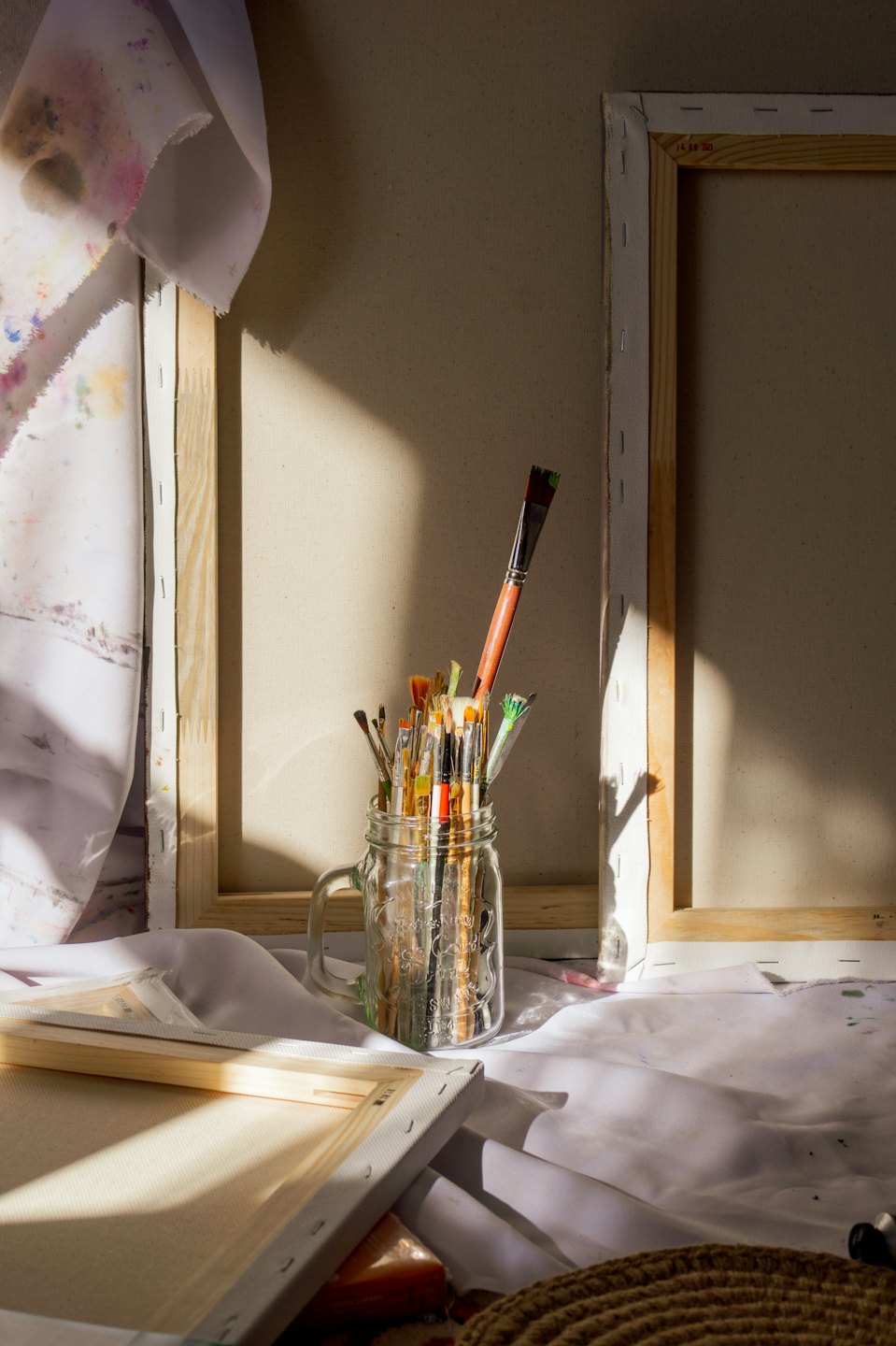 Blank canvases lean against a wall beside a jar of paintbrushes.