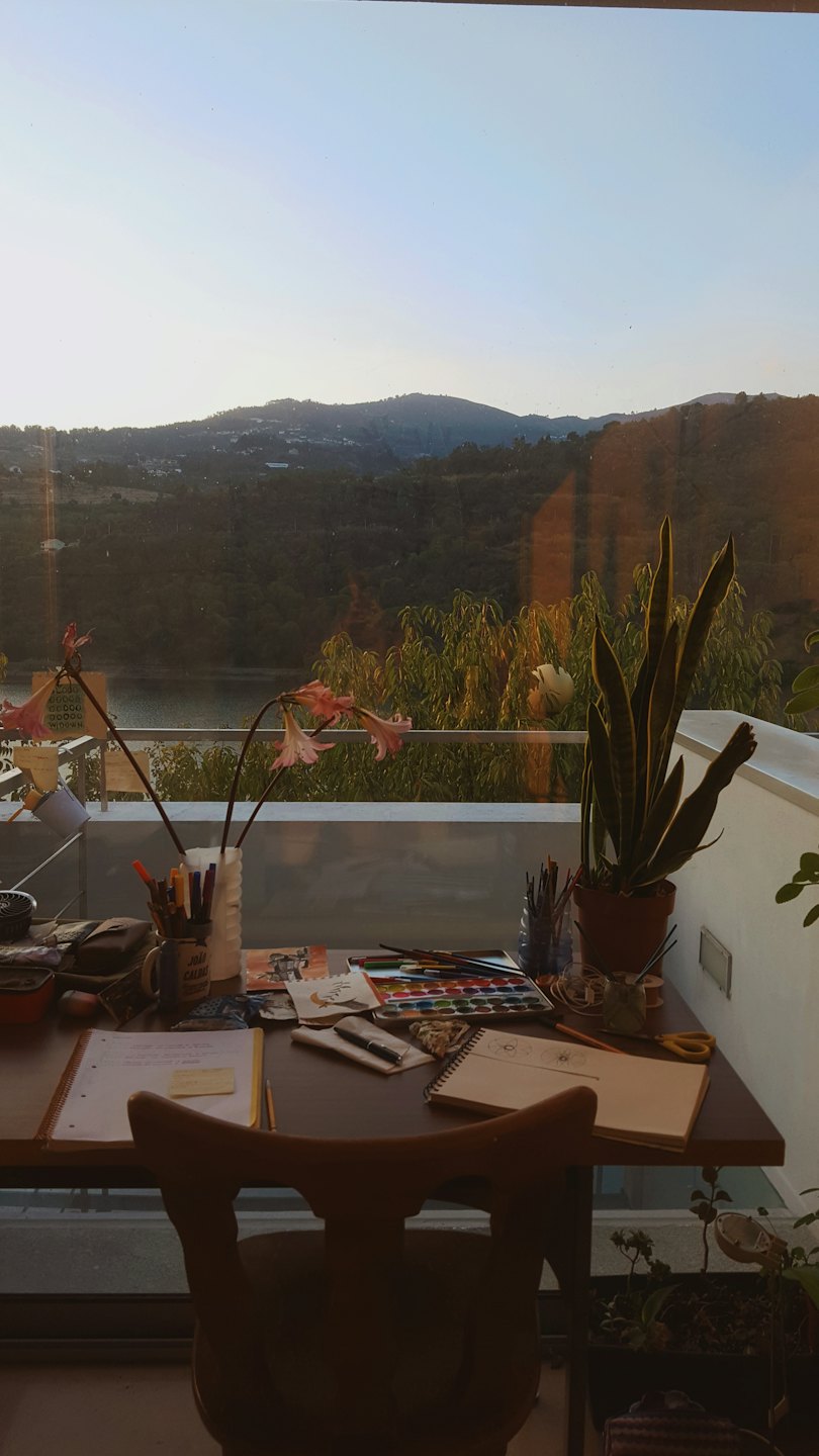 Artist's desk with art supplies and a peaceful landscape outside.